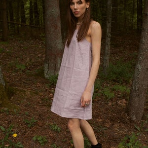 May include: A woman wearing a light purple linen dress and black combat boots stands in a forest.