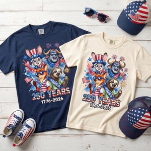 Puede incluir: Una camiseta azul marino y una crema con un gr&aacute;fico de animales de dibujos animados con atuendo patri&oacute;tico, sosteniendo banderas estadounidenses y bengalas. El texto dice 250 YEARS 1776-2026. Incluye dos gorras de b&eacute;isbol y un par de zapatillas.