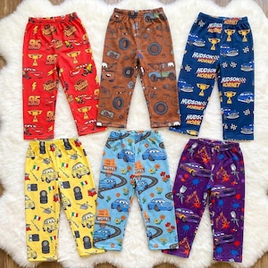 Puede incluir: Seis pantalones con varios estampados de personajes de la pel&iacute;cula Cars. Los pantalones son rojos, marrones, azules, amarillos, azul claro y morados, cada uno con cintura el&aacute;stica y un patr&oacute;n repetitivo de veh&iacute;culos, neum&aacute;ticos y trofeos.