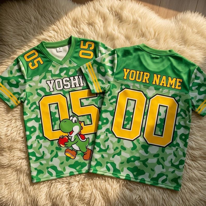 May include: Two green and white camouflage patterned jerseys with yellow accents. The left jersey features the text YOSHI, the number 05, and a graphic of a green dinosaur holding a red apple. The right jersey displays the text YOUR NAME and 00.