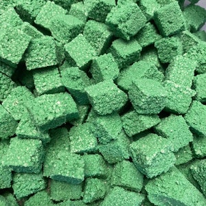 May include: A close-up of a pile of small, green, cube-shaped sponges. The sponges are made of a porous material and have a rough texture.