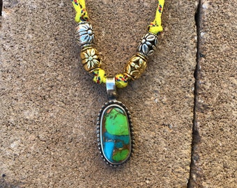 May include: A green and blue turquoise stone pendant necklace with silver and gold accents. The necklace is made with yellow and red rope.