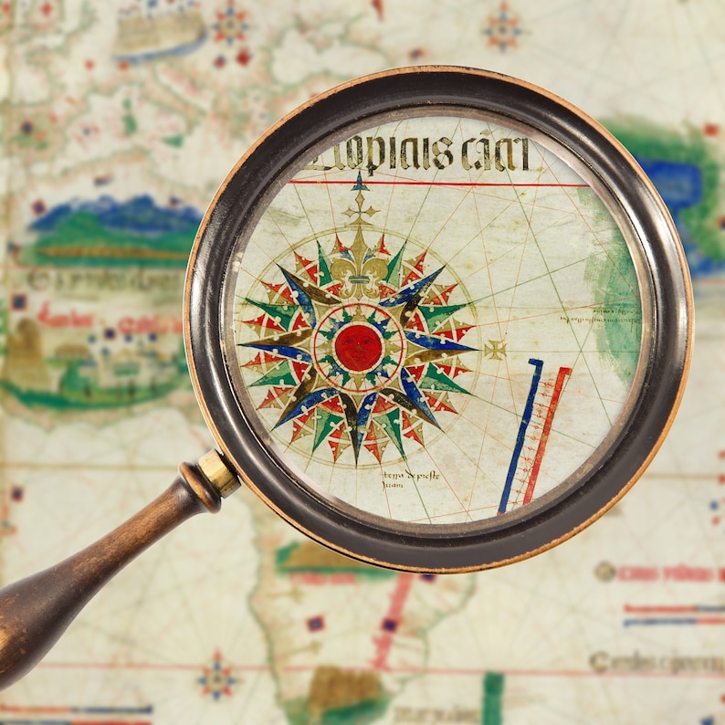 May include: A magnifying glass with a wooden handle is positioned over a vintage map. The map features a compass rose with a colorful design and the text "Topias Cani".