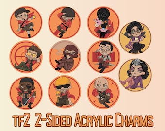 May include: A collection of eleven circular acrylic charms featuring chibi-style characters from Team Fortress 2, including the Scout, Soldier, Pyro, Sniper, Spy, Medic, Demoman, Engineer, Heavy, Administrator, and Miss Pauling. Text reads: TF2 2-SIDED ACRYLIC CHARMS.