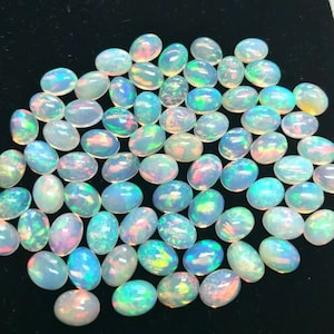 Puede incluir: Una colección de piedras preciosas de ópalo de forma ovalada e iridiscentes. Los ópalos son una mezcla de blanco, azul, verde y rosa.