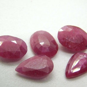May include: Five faceted ruby gemstones in various pear and oval shapes. The gemstones are a deep pink color and have a high shine.