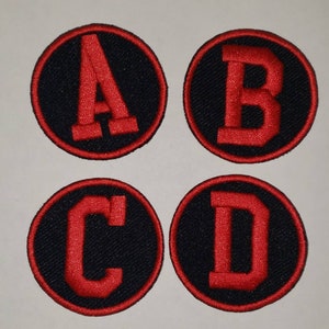 May include: Four round black fabric patches with red embroidered letters A, B, C, and D.