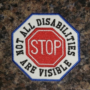 May include: Embroidered patch with a white background and a blue border. The patch features a red octagon with the word "STOP" in white. The text "NOT ALL DISABILITIES ARE VISIBLE" is arched around the octagon.