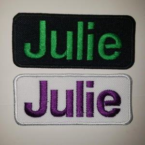 May include: Two embroidered patches with the name "Julie" on them. One patch is black with green lettering and the other is white with purple lettering.