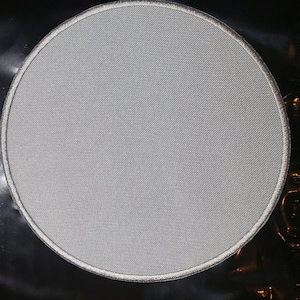 May include: A white, round, blank patch with a silver embroidered border.