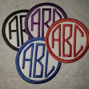 May include: Four embroidered fabric patches with white backgrounds and black, purple, red, and blue stitching. Each patch features the letters "ABC" in a circular design.