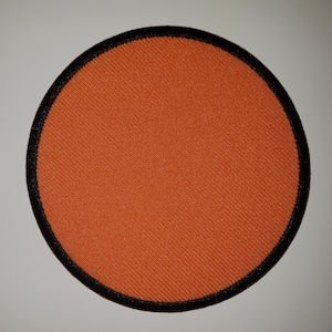 May include: A round, orange fabric patch with a black border. The patch is blank and ready to be customized.