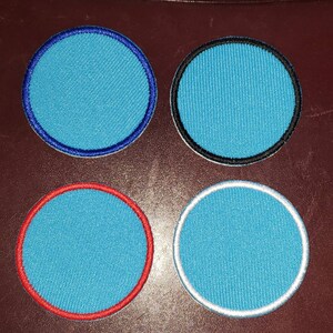 May include: Four round patches with a light blue center and a colored border. The borders are blue, black, red, and white. The patches are made of a textured fabric.