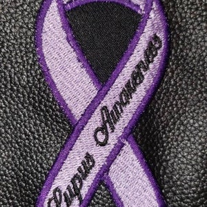 May include: Purple ribbon with the words "Lupus Awareness" embroidered on it.