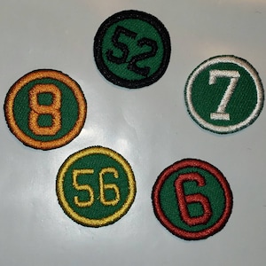 May include: Five embroidered patches with different numbers on them. The patches are circular and have a green background with a white or orange border. The numbers are 52, 7, 8, 56, and 6.
