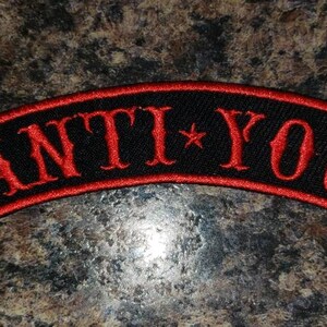 May include: A black and red embroidered patch with the text "ANTI*YOU" in white lettering.