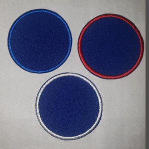 May include: Three circular patches with a blue fabric center. One patch has a blue border, another a red border, and the third a silver border. The patches are arranged in a triangular pattern against a light gray background.