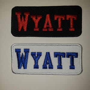 May include: Two embroidered patches with the name "WYATT" in red and blue lettering. The top patch is black and the bottom patch is white.