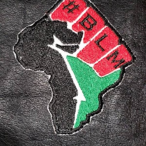 May include: Black leather patch featuring a stylized map of Africa with a raised fist, and the letters BLM in red. The patch has green and white accents and is embroidered.