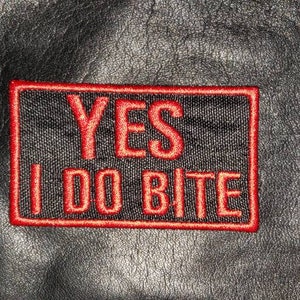 May include: A black leather patch with red stitching. The patch says "YES I DO BITE".