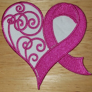 May include: Pink ribbon in the shape of a heart with a white background and a swirl design. The ribbon is a symbol of breast cancer awareness.