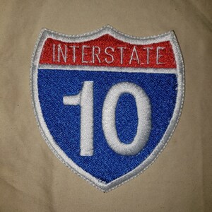 May include: A blue and red interstate highway sign with white text and the number 10.