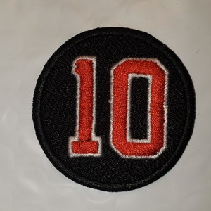 May include: A black and white circular patch with the number 10 embroidered in red.