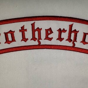 May include: Embroidered patch with the word "Brotherhood" in red gothic lettering on a white banner with a red border. The patch has a curved shape and is likely for a jacket or vest.
