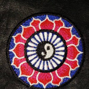May include: Embroidered patch featuring a yin-yang symbol at the center, surrounded by a floral design in red, white, and blue. The patch is circular and set against a black background.
