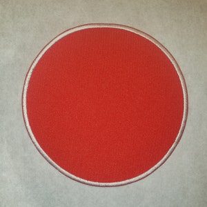 May include: A red circle with a white outline. The circle is made of fabric and has a textured surface.