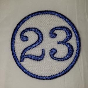 May include: A white circle with a blue border and the number 23 in blue embroidery.
