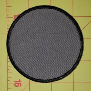 May include: A gray fabric circle patch with a black border. The patch is about 2 inches in diameter.