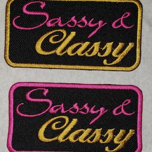 May include: Two black fabric patches with gold and pink embroidery. The patches read "Sassy & Classy".