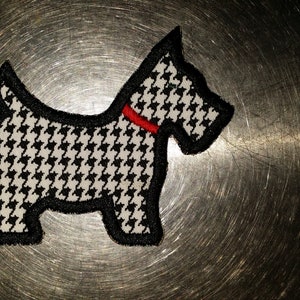 May include: Black and white houndstooth dog patch with a red collar. The patch is on a silver background.