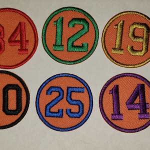 May include: Six round orange fabric patches with different numbers embroidered in various colors. The numbers are 34, 12, 19, 30, 25, and 14.