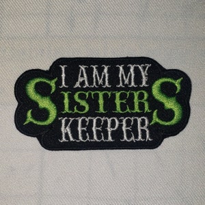 May include: Black embroidered patch with green lettering that reads "I am my sister's keeper".