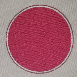 May include: A round, magenta-colored patch with a white embroidered border. The patch has a textured fabric appearance and is set against a white background.