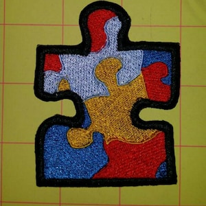 May include: A colorful embroidered puzzle piece patch with red, blue, yellow, and white sections. The patch is outlined in black.