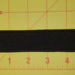 May include: A black rectangular patch of fabric, approximately 5 inches long, with a textured surface.