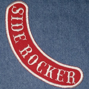 May include: A red, curved embroidered patch with the words "SIDE ROCKER" in white, outlined in white. The patch is set against a blue denim background.