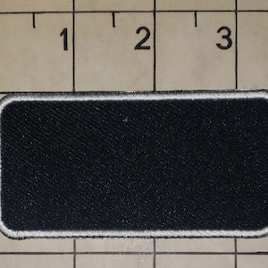 May include: A black rectangular patch with a white border. The patch is made of a textured fabric.