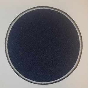 May include: A dark blue round patch with a white border. The patch is made of fabric and has a smooth surface.