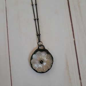 May include: A delicate white flower pendant necklace with a black chain. The flower is made of glass and has a raised design. The chain is made of metal and has a ball chain style.