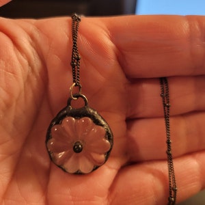 May include: A delicate silver chain necklace with a pendant featuring a pink flower design. The flower is made of glass and has a raised centre.