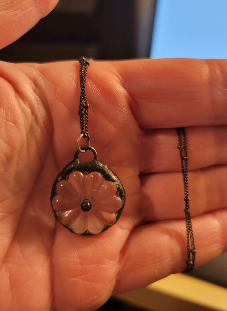 May include: A delicate silver chain necklace with a pendant featuring a pink flower design. The flower is made of glass and has a raised centre.