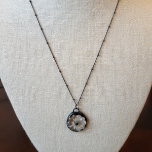 May include: A black chain necklace with a white flower pendant. The flower is carved into a round, clear glass piece.