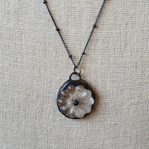 May include: A black chain necklace with a clear glass flower pendant. The flower has a black centre.