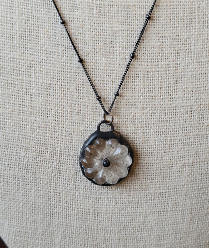 May include: A black chain necklace with a clear glass flower pendant. The flower has a black centre.
