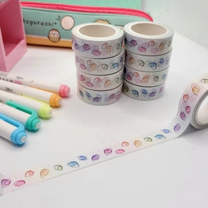 May include: A set of six rolls of washi tape with a grid pattern and colorful eye designs. The tape is unrolled and laid out on a white surface.