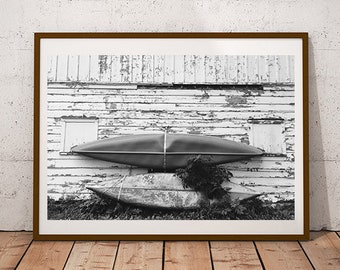 May include: Black and white photograph of two wooden canoes hanging on a weathered wooden wall. The canoes are stacked on top of each other, with the top canoe partially obscured by the bottom canoe. The wall is made of horizontal planks, and the wood is weathered and worn. The image is in a brown frame.